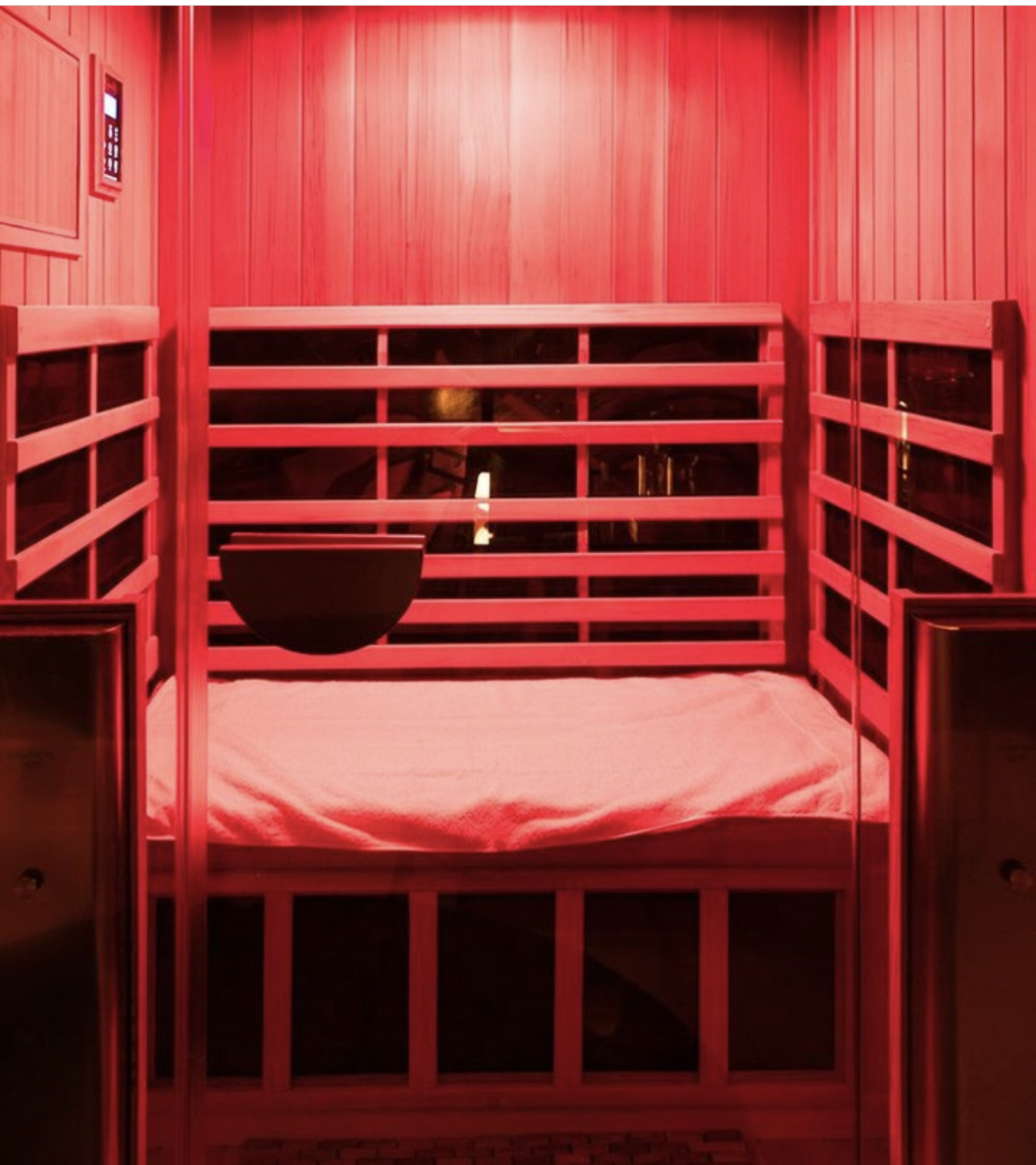 A private infrared sauna room glowing red, with a fresh towel laid on the bench
