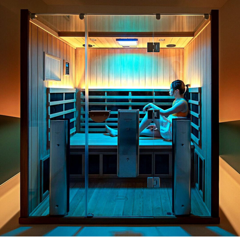 Guest relaxing in infrared sauna with blue chromotherapy lighting at Infrared Sauna Studios